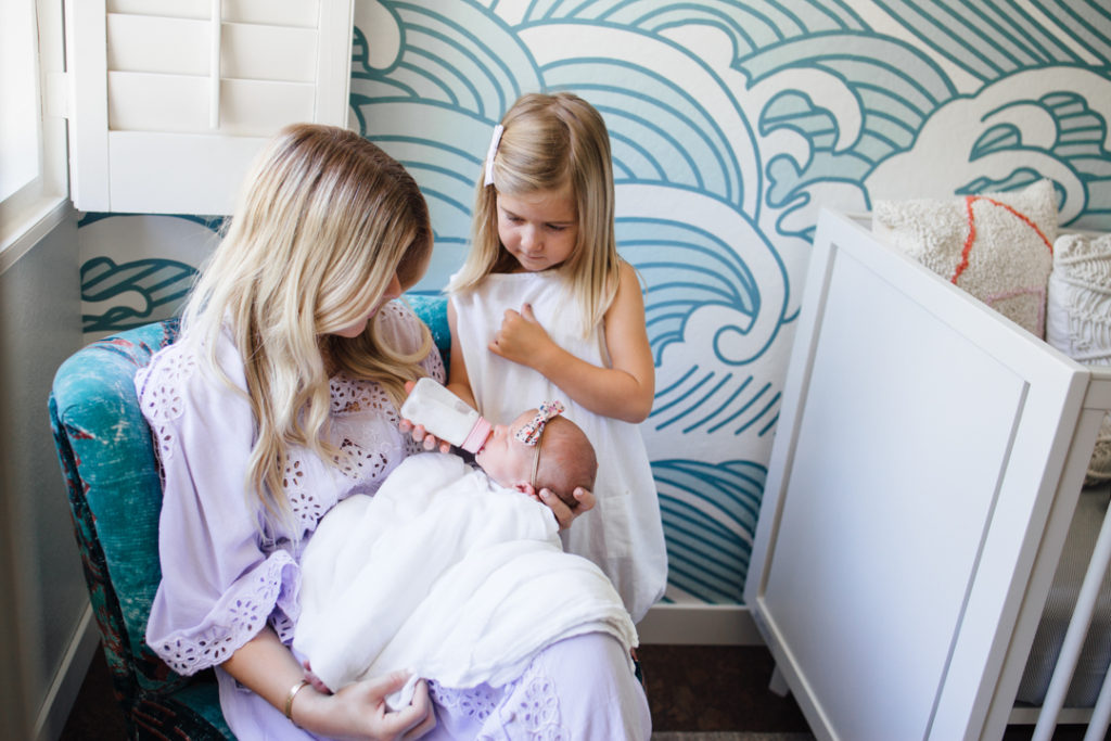 woman feeding a newborn in the nursery while a young girl looks on