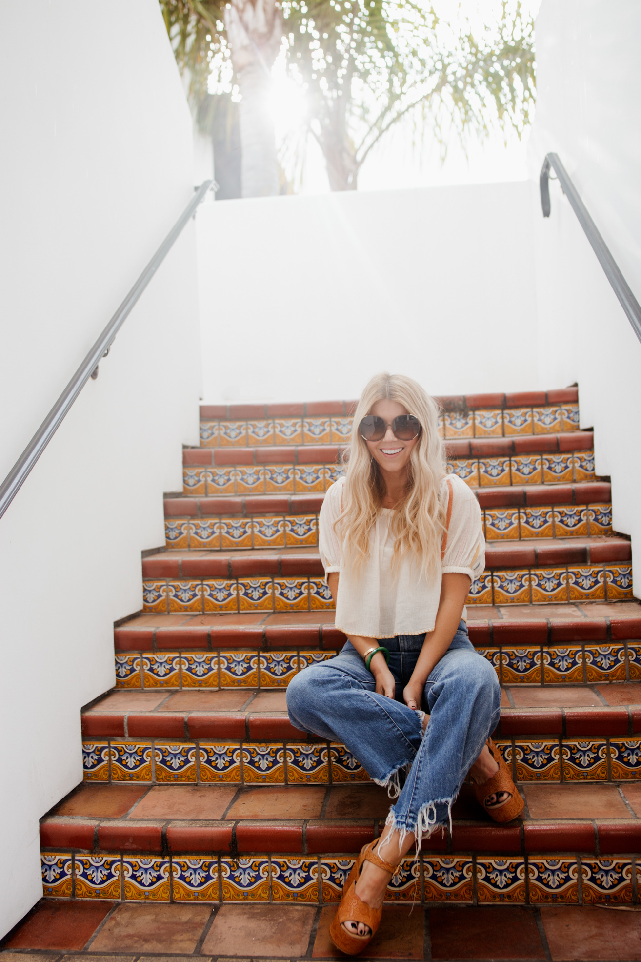 lisa allen of salty lashes sitting on the stairs and wearing a UO peasant top one of her tops for summer with DL1961 jeans, free people wedges and chloe sunglasses