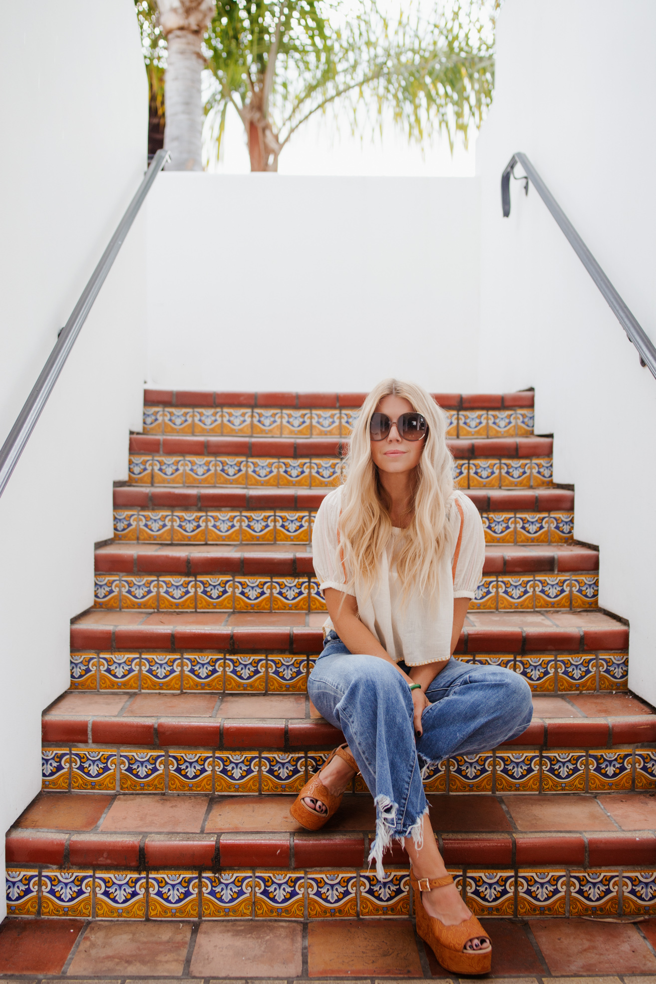 lisa allen of salty lashes wearing a UO peasant top one of her tops for summer  with DL1961 jeans, free people wedges and chloe sunglasses and sitting on the stairs