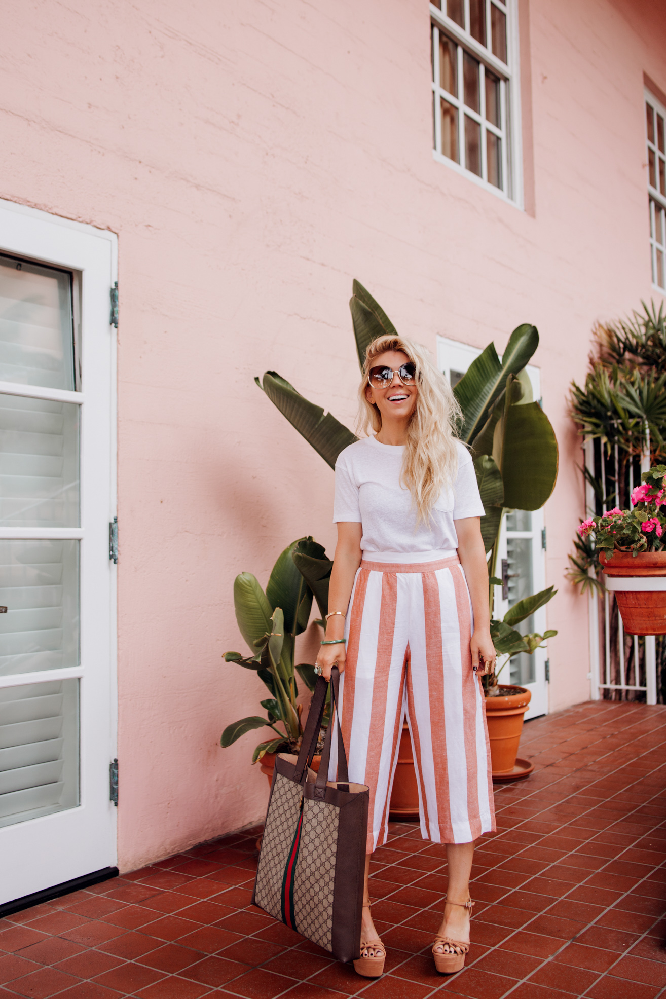 Fashion blogger Lisa Allen of Salty Lashes styles Madewell wide leg pants with a fitted white bodysuit, Free People platforms, Gucci tote, and Chloe sunglasses in La Jolla, California.