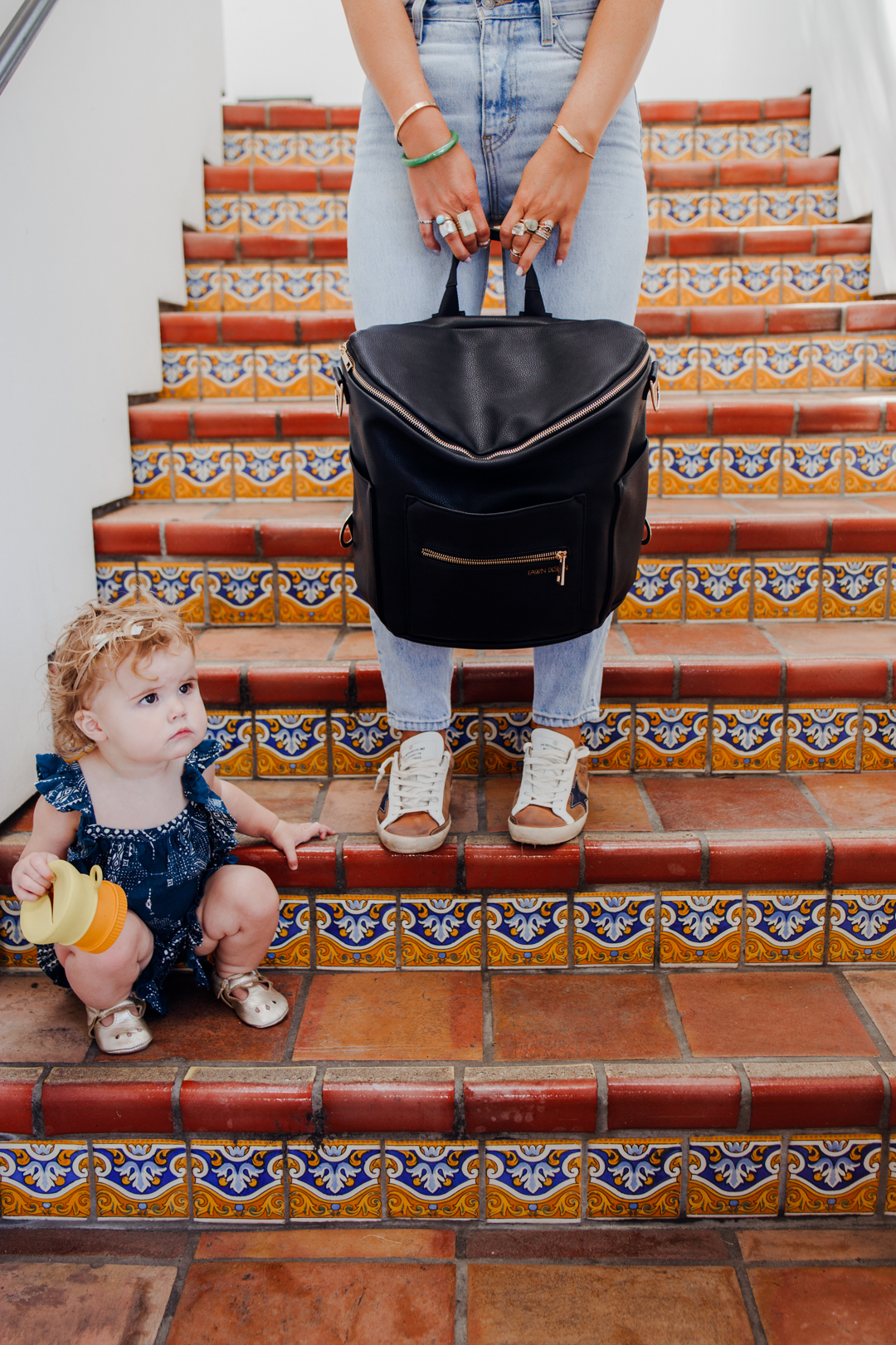 Lisa Allen holding a black faux-leather backpack with gold zippers
